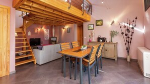 A cozy interior with a wooden dining table, chairs, a sofa, and a staircase leading to an upper level. - La Roche Cozy Forest Escape (Marcouray)