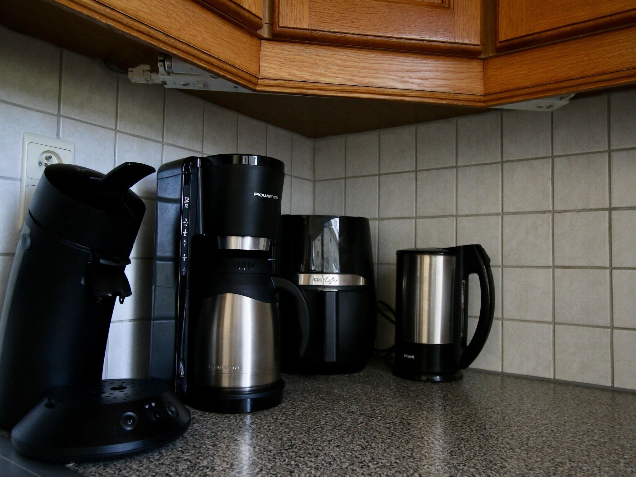 A kitchen with a coffee maker, a kettle, and a mug on the counter.