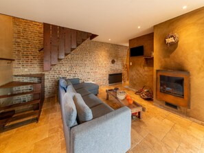 A modern living room with a brick wall, a fireplace, a sofa, and a staircase. - Bertrix charming 2-bedroom holiday home (Bertrix)