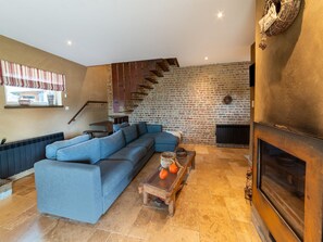 A living room with a sectional sofa, a fireplace, a brick wall, and a window with curtains. - Bertrix charming 2-bedroom holiday home (Bertrix)