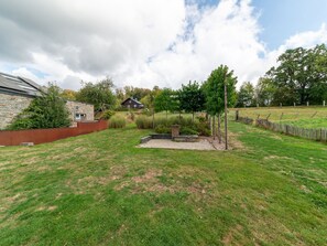 A grassy backyard with a stone wall, a wooden fence, and a small garden area. - Bertrix charming 2-bedroom holiday home (Bertrix)
