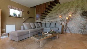 A living room with a grey sectional sofa, a glass-top coffee table, and a brick wall with a wooden staircase.
