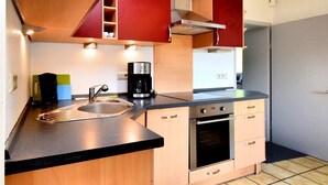 A compact kitchen with a built-in oven, a coffee maker, and wooden cabinets.