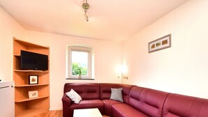 A living room with a red leather sofa, a white coffee table, and a TV on a wooden shelf.