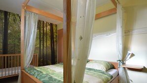 A four-poster bed with a canopy, a wooden headboard, and a view of a forest through the window. - Holiday Home in Burg Reuland (Burg Reuland)