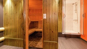 A wooden sauna with a tiled floor, a shower area with a glass door, and a small bench.