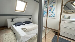 Un dormitorio con cama, lámpara de noche, ventana, cuadro, espejo y cómoda.