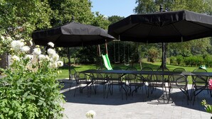 An outdoor patio with a table and chairs, covered by umbrellas, and a swing set in the background. - Modern Cottage with Private Garden in Waimes (Waimes)