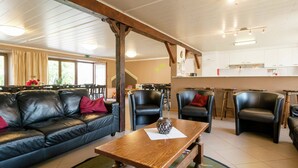 A cozy restaurant with a wooden table, leather sofas, and a kitchen area in the background. - Modern Cottage with Private Garden in Waimes (Waimes)