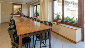 A long dining table with chairs, a large mirror, and potted plants by the windows. - Modern Cottage with Private Garden in Waimes (Waimes)