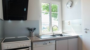 Une cuisine équipée d’une cuisinière, d’un lave-vaisselle et d’une fenêtre donnant sur un espace verdoyant.