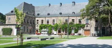 A historic stone building with a symmetrical facade, large windows, and a central courtyard with a fountain.