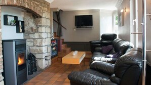 Un salon chaleureux avec une cheminée en pierre, un canapé en cuir et un téléviseur à écran plat fixé au mur.