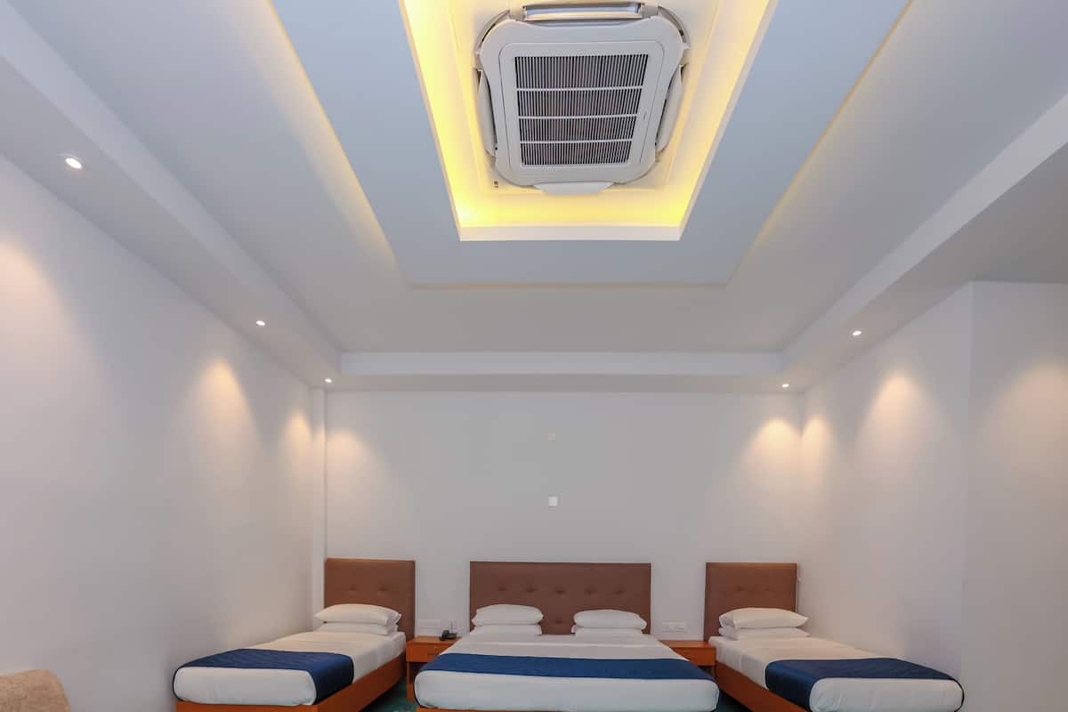 Une chambre d’hôtel avec trois lits, un canapé, une table avec un plateau en verre et un climatiseur au plafond.