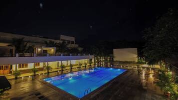 A rectangular swimming pool with a tiled deck surrounding it, located in a courtyard with a modern building in the background.
