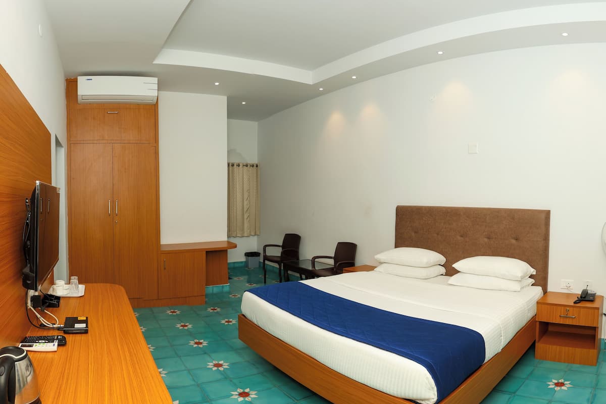 Une chambre d’hôtel équipée d’un lit, d’une table de chevet, d’une télévision, d  ’un bureau, d’une chaise et d’un ventilateur sur pied.