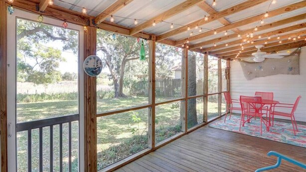 A covered patio with wooden beams, string lights, and a view of a backyard. - Marsh Magic 2 Bed 1 Bath Beach House w Marsh View (Tybee Island)