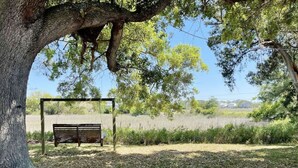 A park bench under a tree with a grassy area and a fence in the background. - Marsh Magic 2 Bed 1 Bath Beach House w Marsh View (Tybee Island)