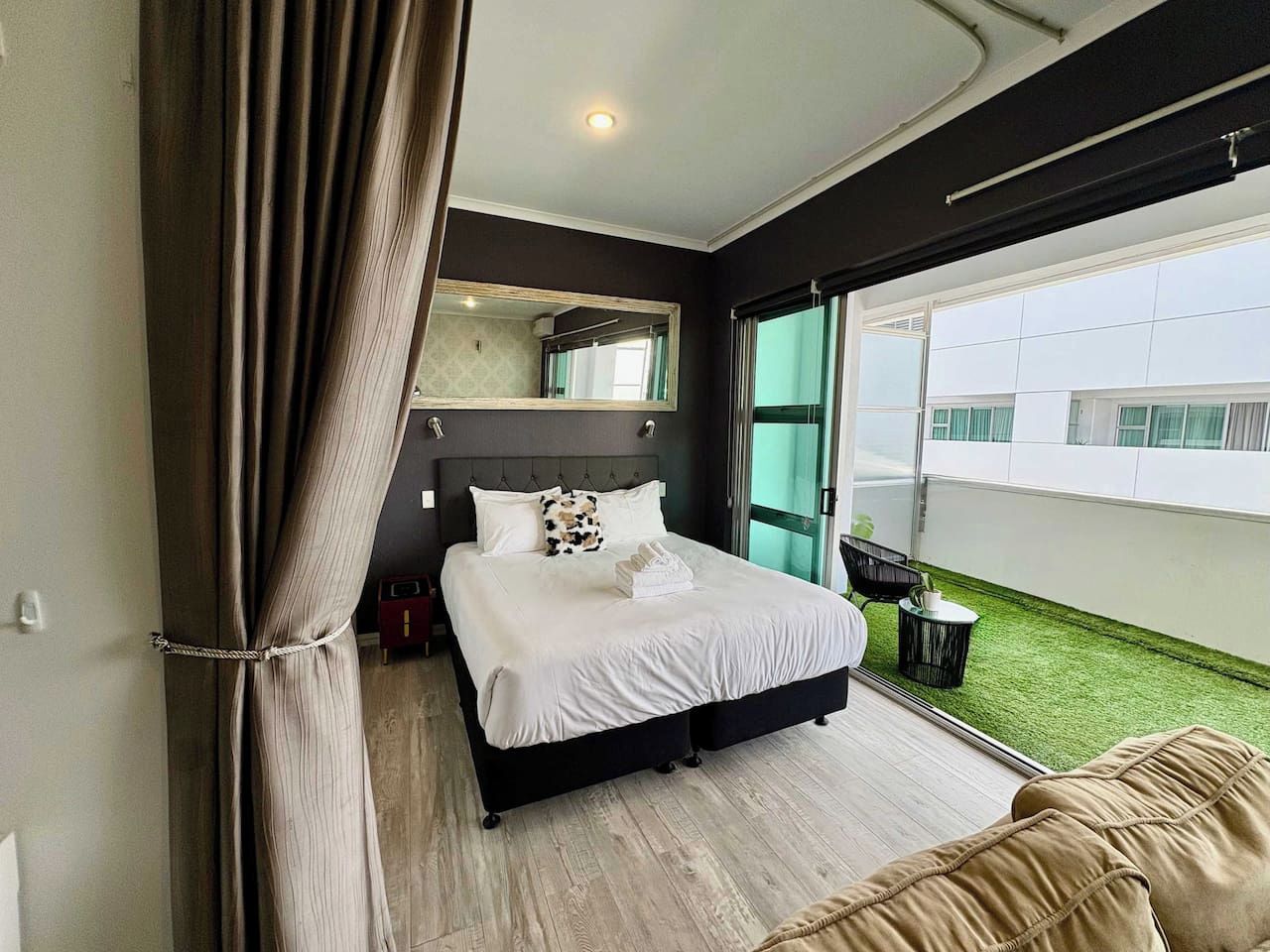 Un dormitorio moderno con una cama grande, una mesita de noche, un espejo y vistas a un área verde al aire libre.