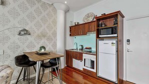 Eine kleine Küche mit Esstisch, Stühlen, einer Mikrowelle, einem Kühlschrank und Holzschränken.