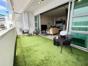 A balcony with artificial grass, a seating area with chairs, and a view of a building with a tower. - Viaduct Studio w/ Balcony Close to Ferry by Zodiak (Auckland)