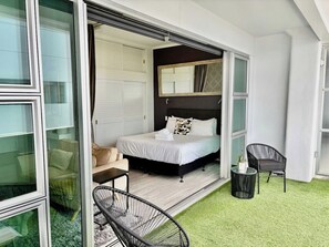 A bedroom with a bed, a chair, a small table, and a sliding glass door leading to a balcony with artificial grass. - Viaduct Studio w/ Balcony Close to Ferry by Zodiak (Auckland)