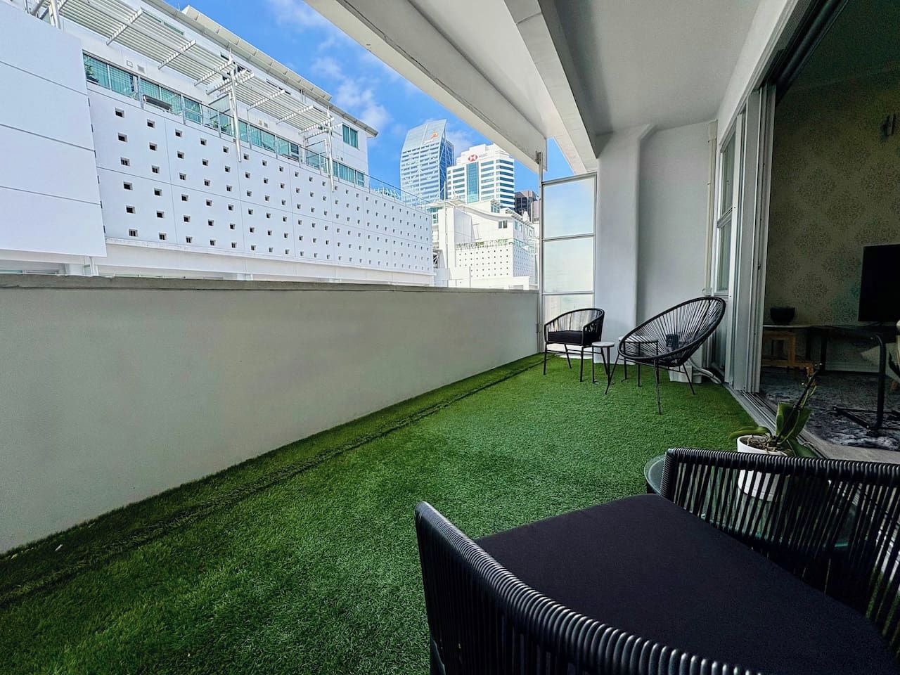 Eine Dachterrasse mit künstlichem Rasen, Gartenmöbeln und Blick auf die Stadt.
