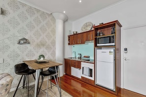 A compact kitchen with a wooden table, two chairs, a microwave, a refrigerator, and a clock on the wall. - Viaduct Studio w/ Balcony Close to Ferry by Zodiak (Auckland)
