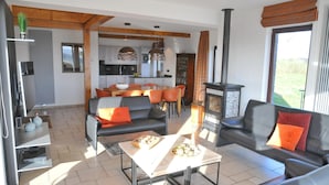 Een moderne woonruimte met een bank, een salontafel en een open haard. Achtergrond toont een keuken met een eettafel en stoelen.