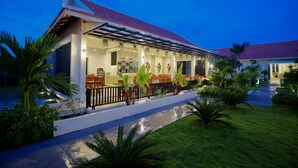 A modern hotel with a covered outdoor seating area, a pool, and lush landscaping. - New Riverside Hotel (Siem Reap)