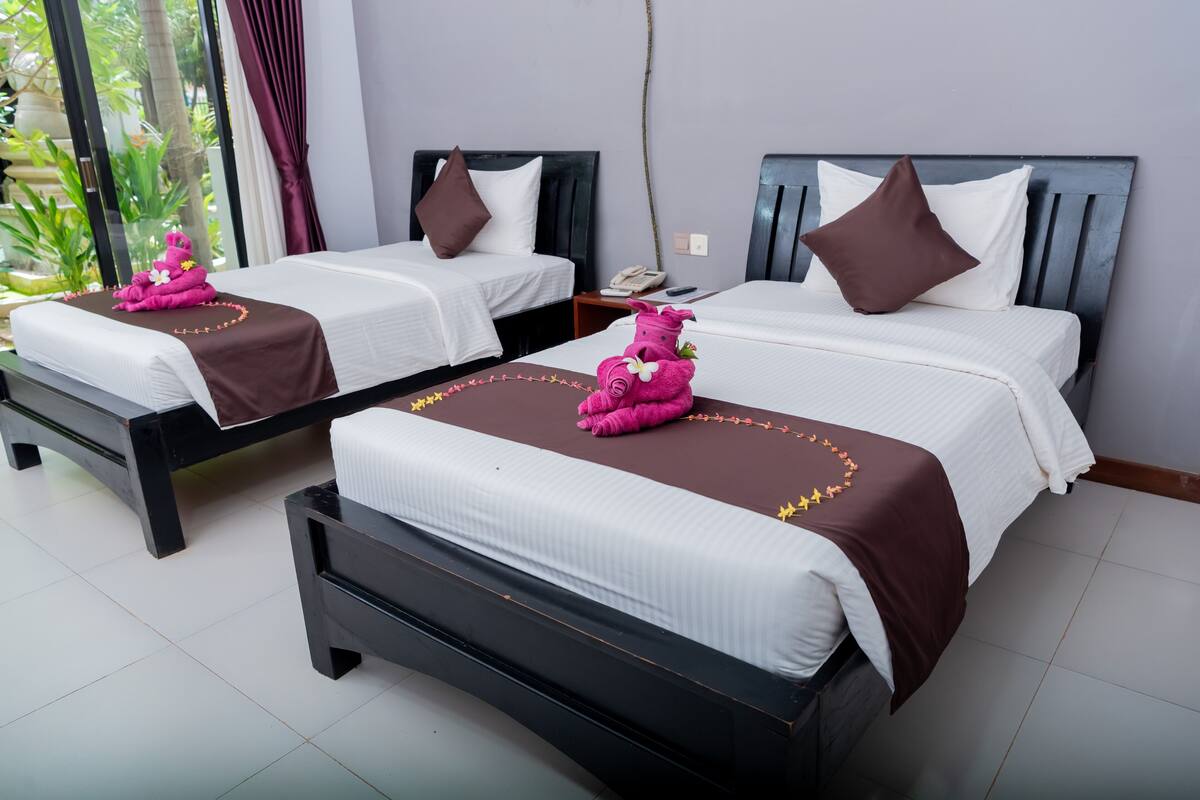 Two twin beds with dark headboards and white bedding, each with a brown decorative pillow and a pink towel with a flower.