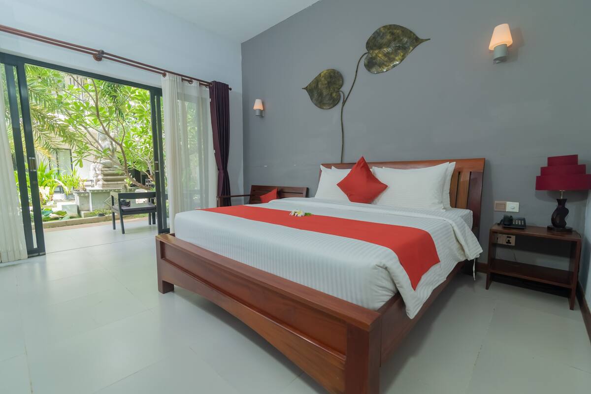 A spacious bedroom with a large bed, a wooden nightstand, and a view of a garden through a sliding door.