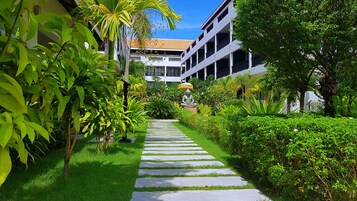 Un sendero conduce a un edificio con una estatua, rodeado de vegetación exuberante y palmeras.