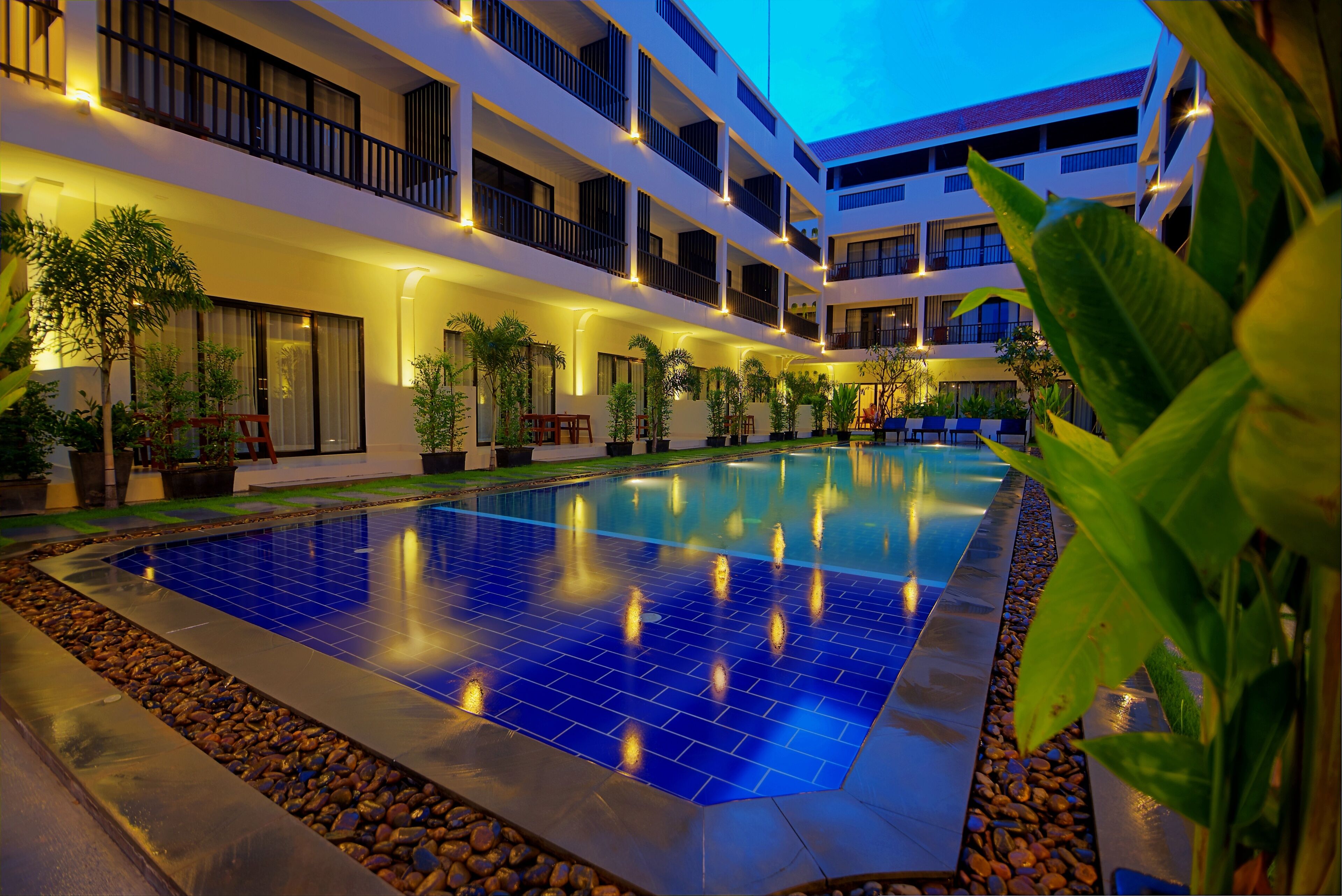 A multi-story hotel with a swimming pool, outdoor seating, and potted plants.