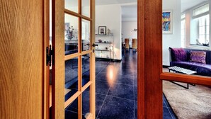 A modern living room with a dark tiled floor, a purple sofa, and a wooden door with glass panels. - Countryside Escape for 9 (Honnay)
