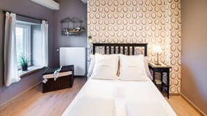 Une chambre d’hôtel comprenant un lit, une table de chevet, une fenêtre avec des rideaux, un radiateur et un mur orné d’un motif circulaire.