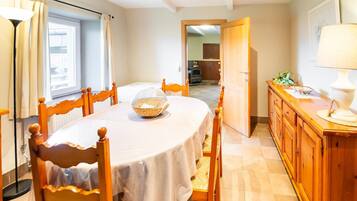 Un coin repas avec une table ronde, des chaises, un bol de collations, une lampe et un meuble en bois.