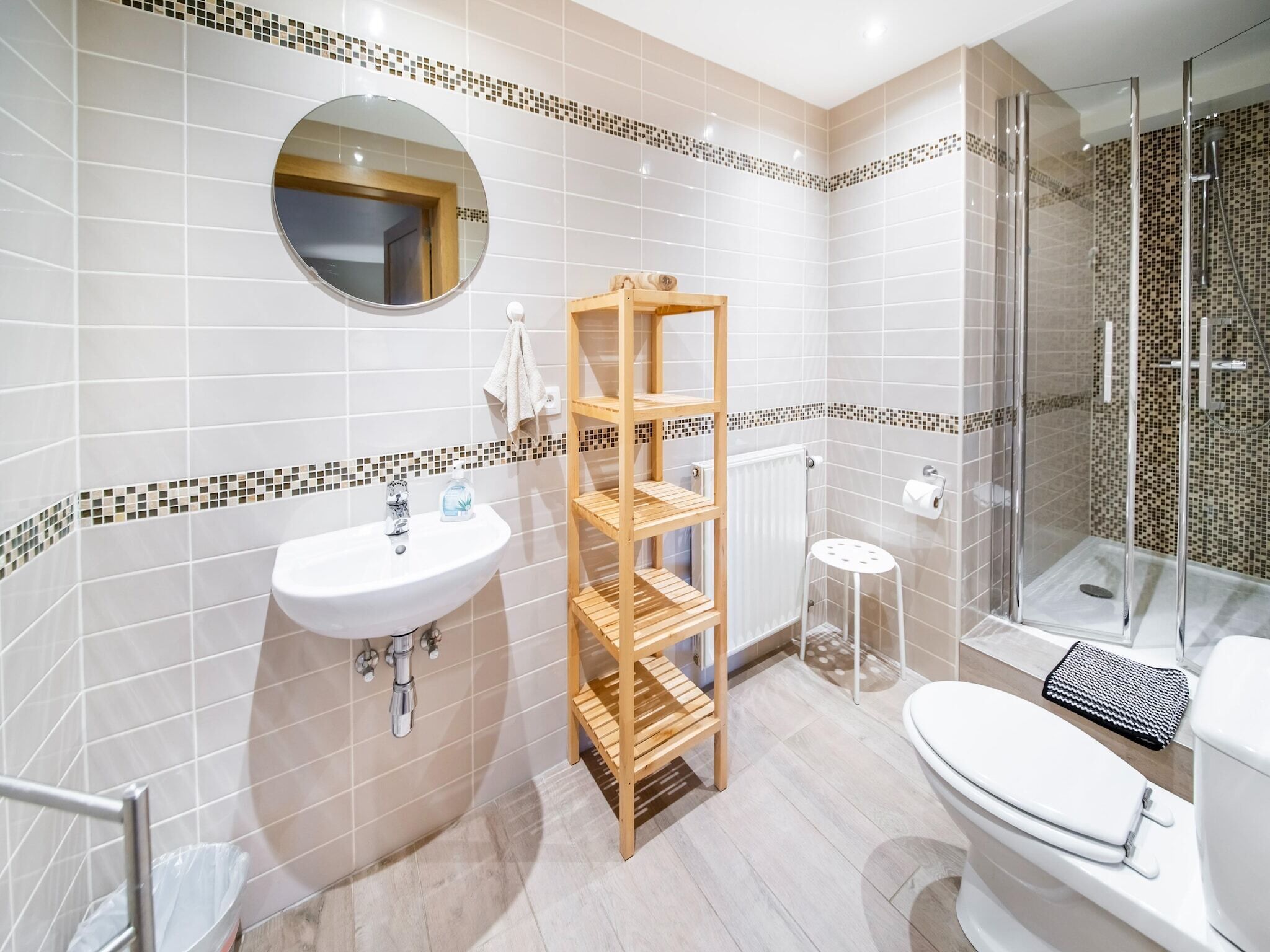 Une salle de bain moderne avec un lavabo blanc, des étagères en bois, une cabine de douche en verre et des toilettes.