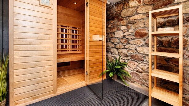 Un sauna en bois avec un mur de pierres en arrière-plan, un banc en bois et une petite étagère.