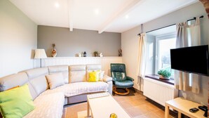 Un salon moderne avec un canapé, un fauteuil vert, une table basse, un téléviseur et une fenêtre avec des rideaux.