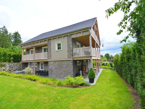 A two-story house with a stone facade, a balcony on the second floor, and a well-maintained lawn. - Luxury Ardennes chalet spa (Septon)