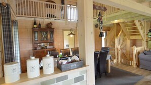 Un interior de cabaña acogedor con comedor, una cocina con armarios de madera y una escalera que conduce a un nivel superior.