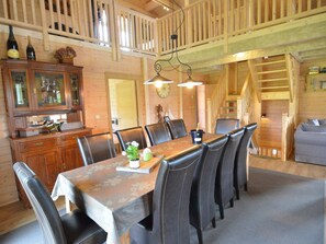 A dining area with a long table, multiple chairs, a wooden cabinet with glass doors, and a staircase leading to an upper level. - Luxury Ardennes chalet spa (Septon)