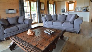 Una sala de estar acogedora con dos sofás grises, una mesa de centro de madera y una cocina al fondo.