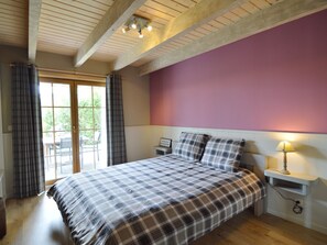 A bedroom with a bed, a nightstand, a lamp, and a window with curtains. - Luxury Ardennes chalet spa (Septon)