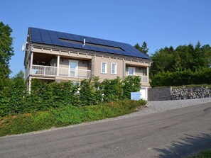 A two-story building with a balcony, solar panels on the roof, and a stone wall. - Luxury Ardennes chalet spa (Septon)