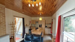 Et moderne interiør med træloft, spiseplads, køkken og udsigt gennem et stort vindue.