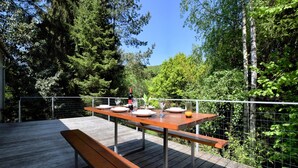 En udendørs træterrasse med et spisebord, omgivet af et wirehegn og frodig vegetation.