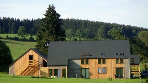 A modern building with a stone facade, wooden exterior, and a large tree in the background. - Beautiful villa with heated outdoor pool (Manhay (lamormenil))
