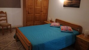 A bedroom with a bed, two pillows, a wooden wardrobe, a chair, and a wall-mounted picture.